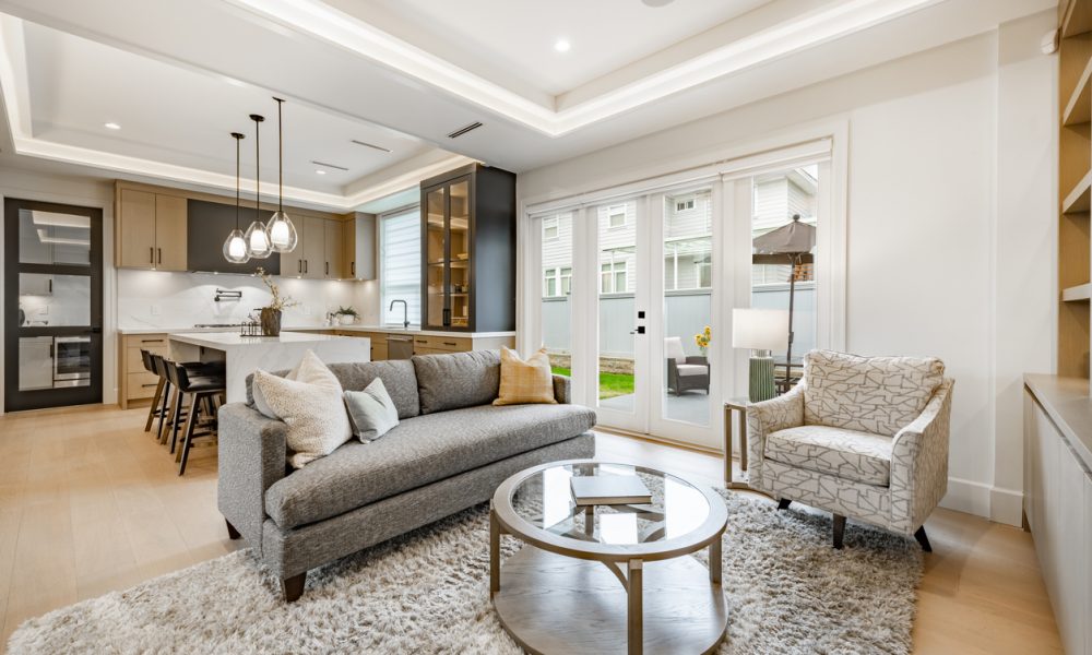 spacious living room in a newly constructed home staged professionally with fireplace view to kitchen grey sofa area rug built in cabinets and shelving recessed lighting in the ceiling modern new furniture
